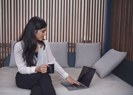 Woman with a coffee working on a laptop from a sofa